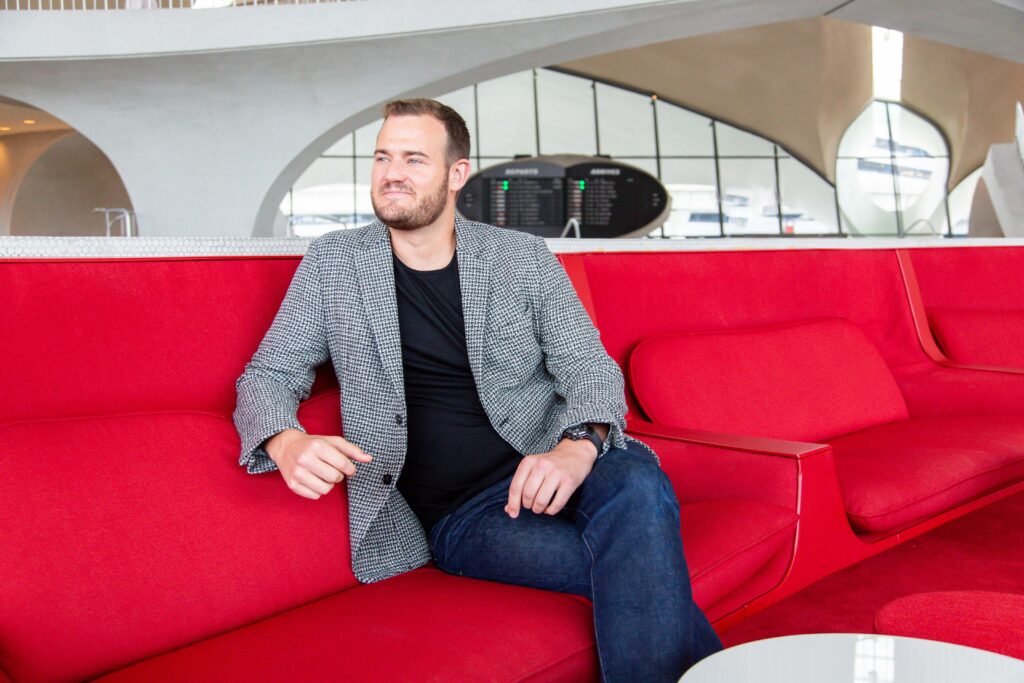 The Points Guy Brian Kelly sitting on a red couch (Photo Credit: The Points Guy)